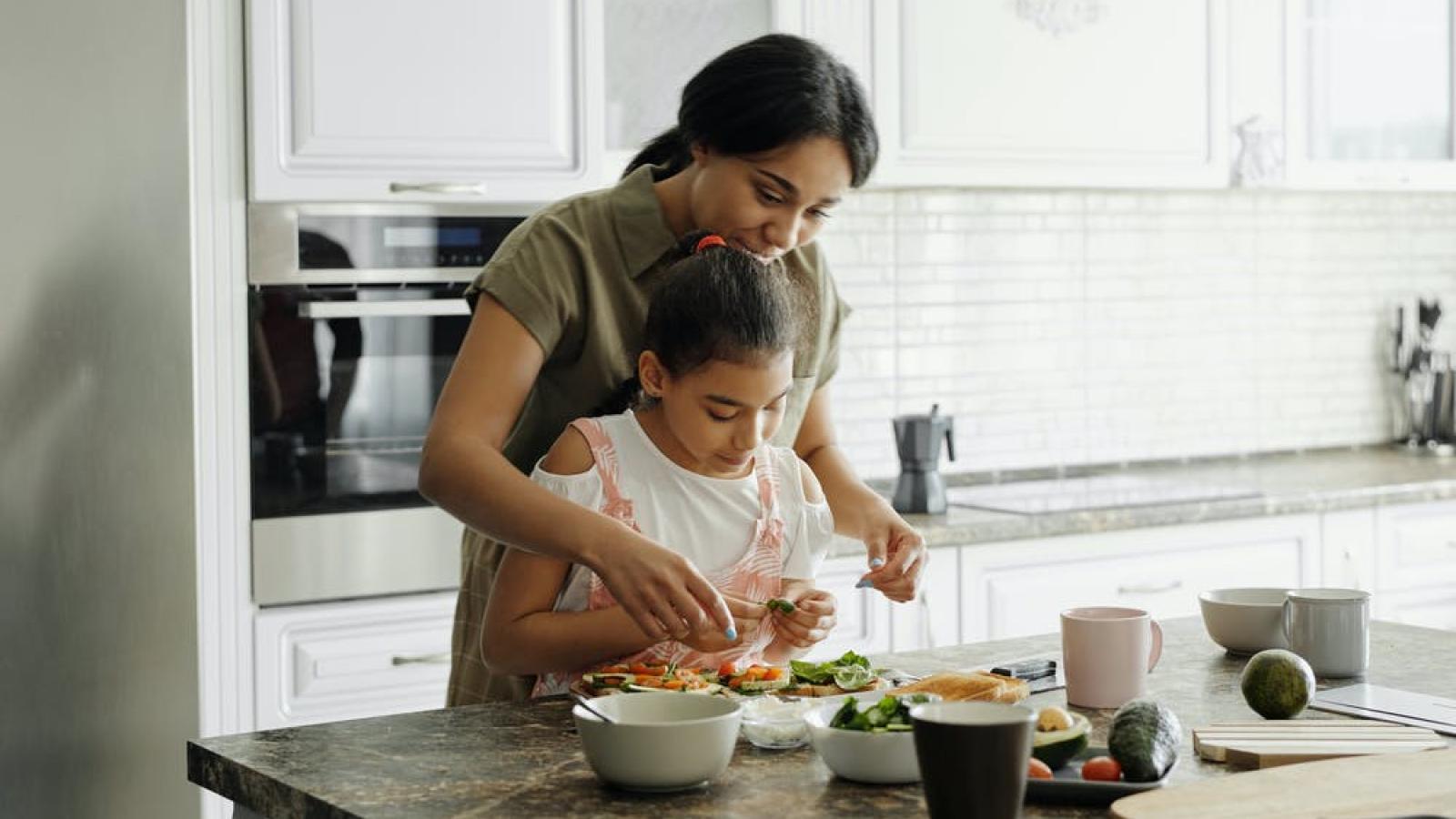 Young girl helping adult woman prepare vegetables